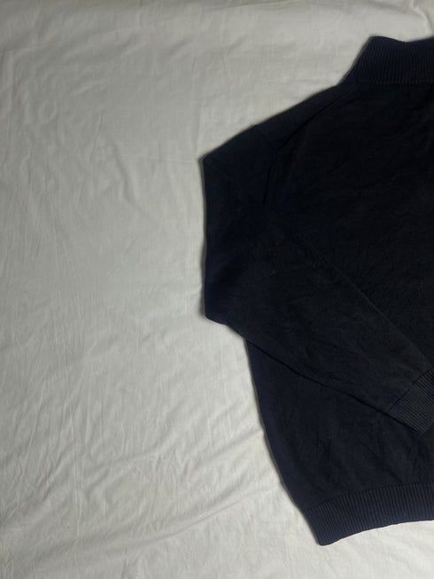 Close-up of vintage Nautica black quarter-zip sweater collar showing grey ribbed lining, size XL tag, silver zipper pull, and embroidered sail chest logo